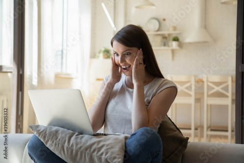 Overjoyed young woman with open mouth looking at laptop screen, reading good news in email, surprised excited female using computer, win online lottery, great shopping offer, sitting on couch at home