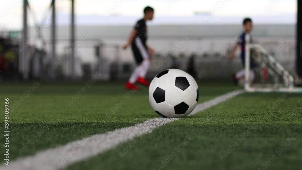 Football on green artificial turf with blurry kid soccer team training. Blurry soccer player training with coach in soccer academy. Football on green artificial turf with blurry kid soccer team training. Blurry soccer player training with coach in soccer academy.