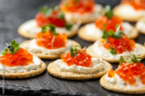 Salmon caviar and soft cheese savory crackers with sesame and poppy seeds served on black slate board