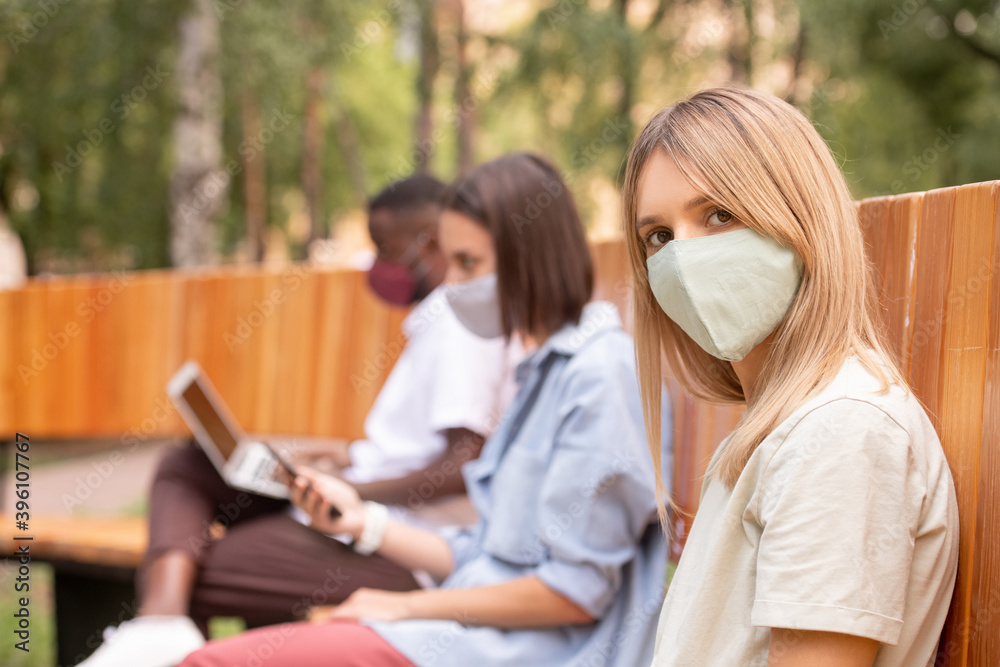 Young blond woman in protective mask looking at you against two millennials Young blond woman in protective mask looking at you against two millennials