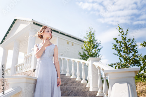 Beautiful girl in tender prom dress on stairs background. Female portrait on spring landscape.