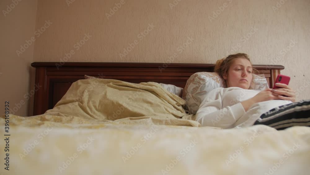 Serious woman with smartphone lying in bed Serious woman with smartphone lying in bed