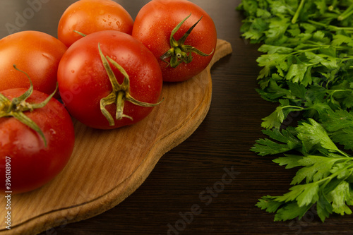 Red tomatoes on a wooden board and a dark textured wood background. With herbs. Eco-friendly tomatoes. Fresh tomatoes. Tomatoes with water drops