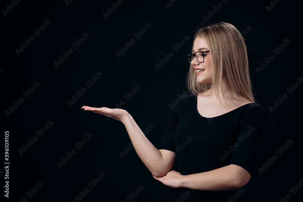 Charming young lady looking at open palm that holding over black background. Pretty woman in eyewear showing empty space for text. Charming young lady looking at open palm that holding over black background. Pretty woman in eyewear showing empty space for text.