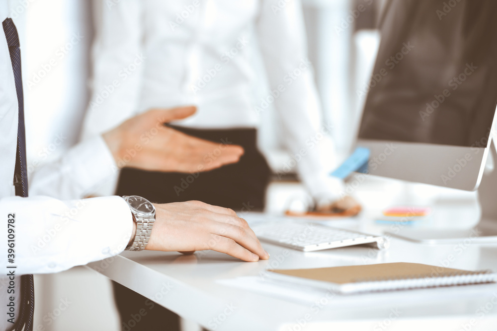 Businessman and woman are discussing questions while using computer and blocknote in modern office, close-up. Teamwork in business Businessman and woman are discussing questions while using computer and blocknote in modern office, close-up. Teamwork in business