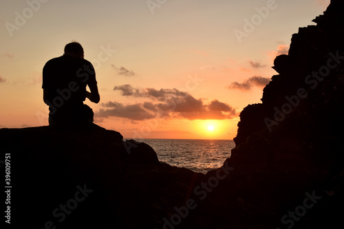 Uomo seduto sugli scogli at tramonto