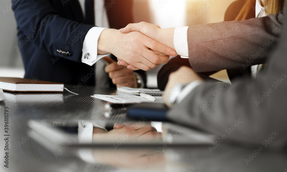 Unknown businessman shaking hands with his colleague or partner above the desk in sunny office, close-up Unknown businessman shaking hands with his colleague or partner above the desk in sunny office, close-up
