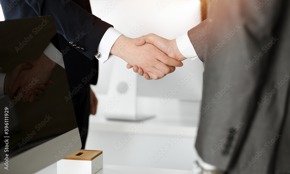 Fototapeta premium Unknown businessman shaking hands with his colleague or partner while standing straight in sunny office, close-up