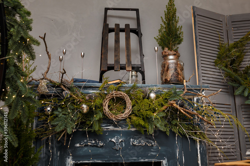 Rustic style Christmas festive decorations, fresh spruce thuja, fir branches, wreath on fireplace, sledges. Warm garland lights boke. Eco-friendly decorative elements. photo