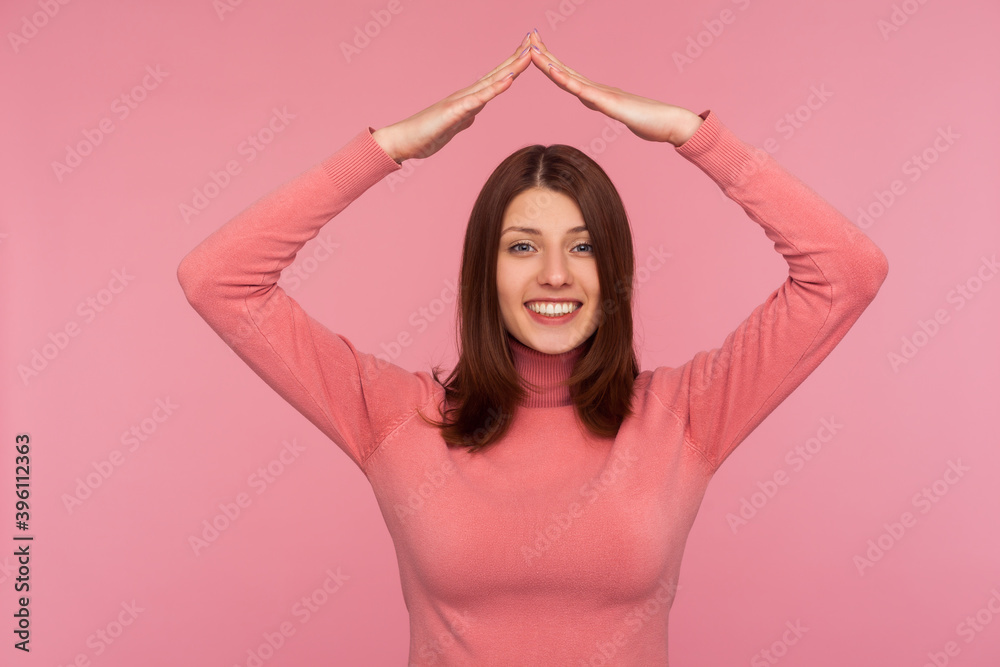 Cheerful woman with brown hair in pink sweater making roof of hands above head looking at camera with toothy smile, feeling herself in safety. Indoor studio shot isolated on pink background Cheerful woman with brown hair in pink sweater making roof of hands above head looking at camera with toothy smile, feeling herself in safety. Indoor studio shot isolated on pink background