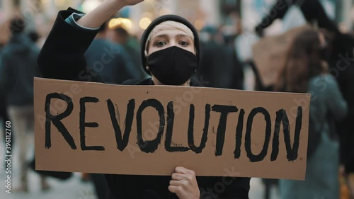 Revoultion concept. Young woman with face mask and banner protesing in the crowd. High quality 4k footage photo