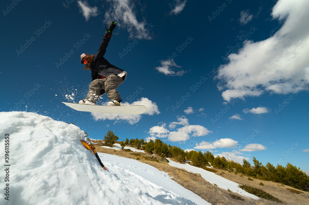 Stylish woman snowboarder makes a trick in flight. Snowboard jump from a kicker against the backdrop of mountains. Freestyle winter sports