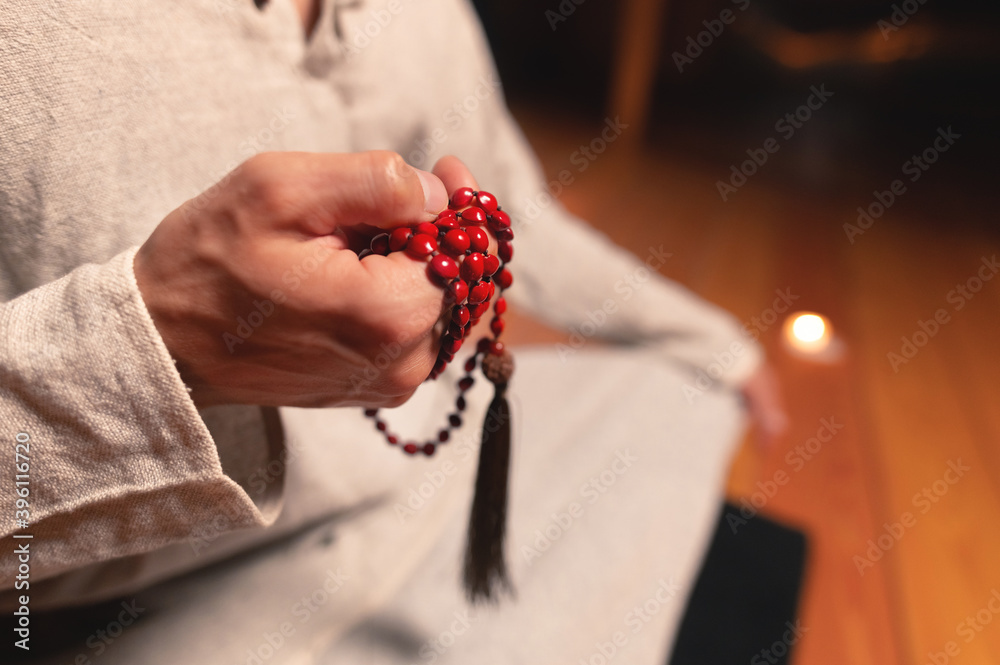 Close-up of a meditating practitioner's hand with a rosary in a dark room Close-up of a meditating practitioner's hand with a rosary in a dark room