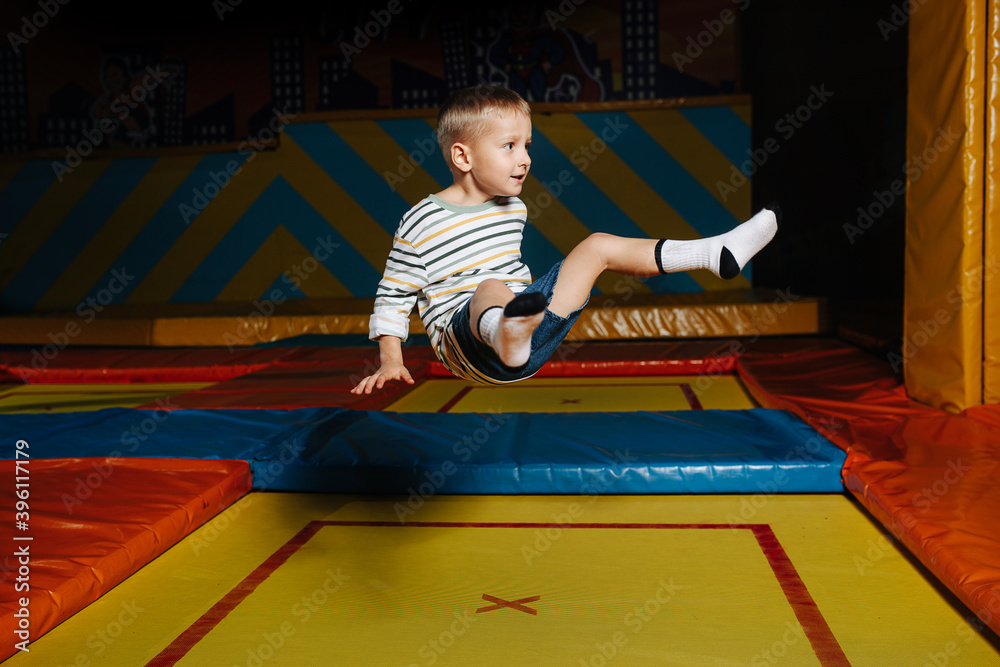 Little boy jumping high on a square trampoline in entertainment center. Hovering in a sitting position.