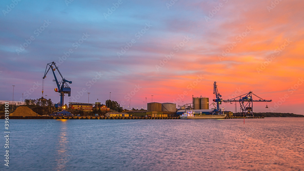 Massive blue cranes unload cargo in a seaportduring sunset