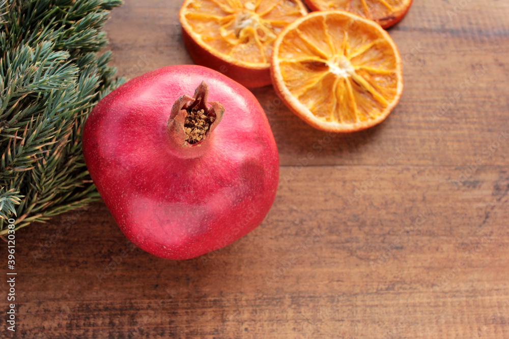 Christmas background with fruits and Christmas tree branches. Pomegranate, dried orange slices and green twigs on wooden table. Flat lay winter holiday composition. Copy space Christmas background with fruits and Christmas tree branches. Pomegranate, dried orange slices and green twigs on wooden table. Flat lay winter holiday composition. Copy space