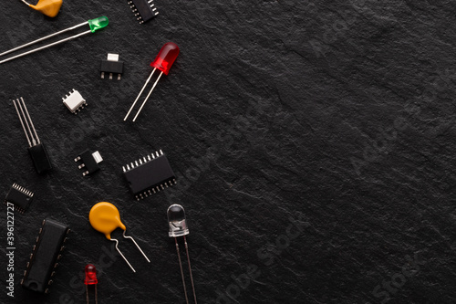Electronic components over black stone background with copy space. There are microcontrollers, transistors, green LEDs, microcircuits, thyristors.