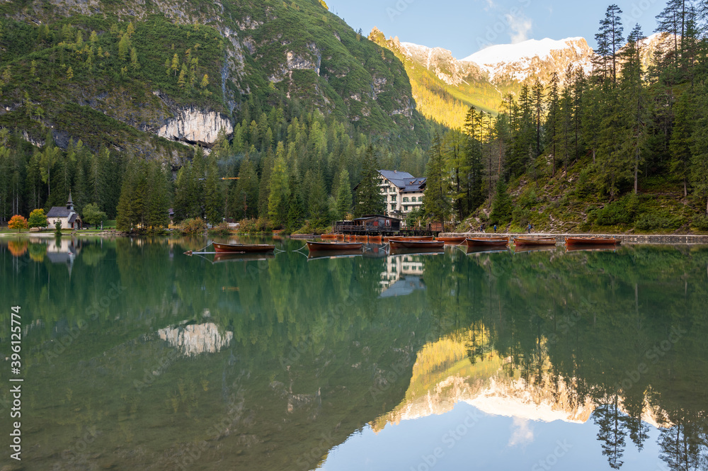 A view of the lake Pragser Wildsee in the Dolomites with a chain of boats, mountains and woods in autumn in South Tyrol, Italy.