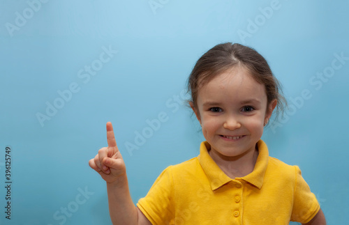 Girl in a yellow T-shirt on a naked background. The child holds a thumb up. Place for your text.