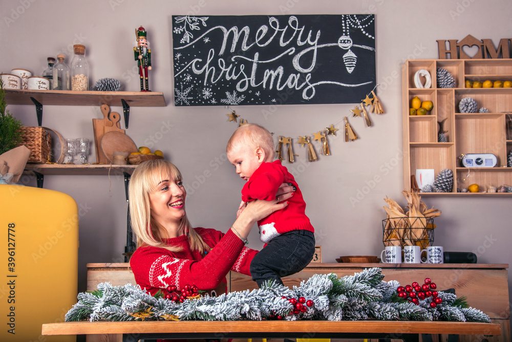 Young attractive smiling woman with her little son in the kitchen in retro loft style waiting for New Year and Christmas, showing cubes with the inscription