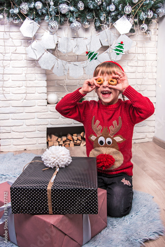 Obraz na płótnie Little cute little girl in Christmas clothes is happy New Year gifts by making round glasses of bagels w salonie