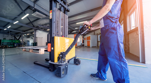 A worker in a warehouse uses a hand pallet stacker to transport pallets.