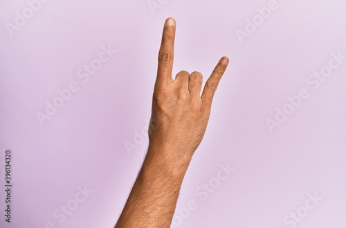 Arm and hand of caucasian young man over pink isolated background gesturing rock and roll symbol  showing obscene horns gesture