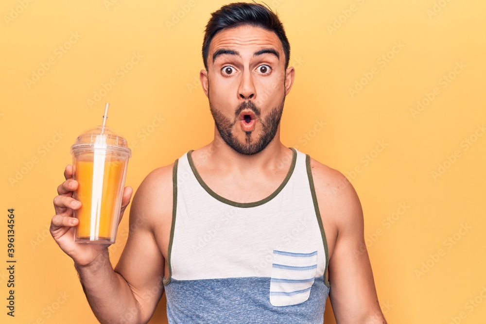 Handsome man with beard wearing sleeveless t-shirt drinking glass of healthy orange juice scared and amazed with open mouth for surprise, disbelief face Handsome man with beard wearing sleeveless t-shirt drinking glass of healthy orange juice scared and amazed with open mouth for surprise, disbelief face