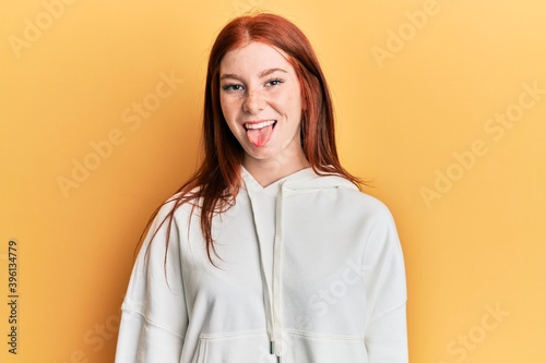 Young red head girl wearing casual sweatshirt sticking tongue out happy with funny expression. emotion concept.