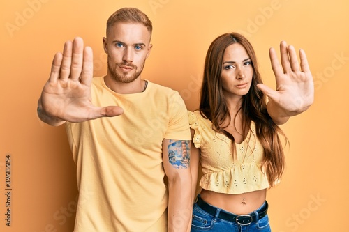 Young couple of girlfriend and boyfriend hugging and standing together doing stop sing with palm of the hand. warning expression with negative and serious gesture on the face.