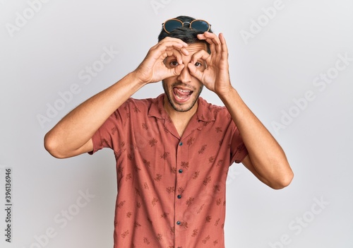 Young handsome man wearing casual summer clothes doing ok gesture like binoculars sticking tongue out, eyes looking through fingers. crazy expression.