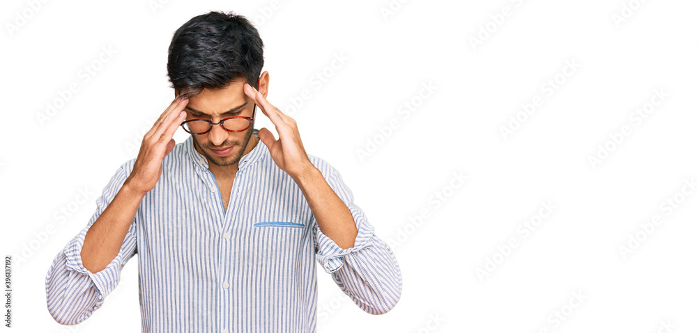 Young handsome man wearing casual clothes and glasses with hand on head for pain in head because stress. suffering migraine. Young handsome man wearing casual clothes and glasses with hand on head for pain in head because stress. suffering migraine.