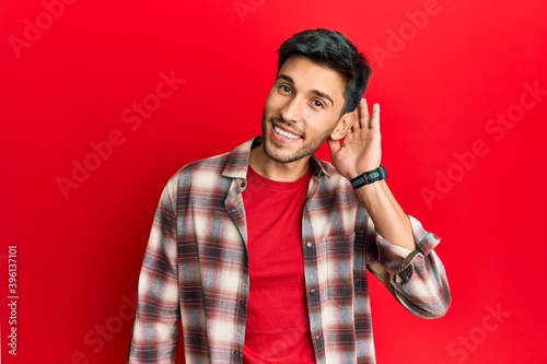 Young handsome man wearing casual clothes smiling with hand over ear listening and hearing to rumor or gossip. deafness concept.