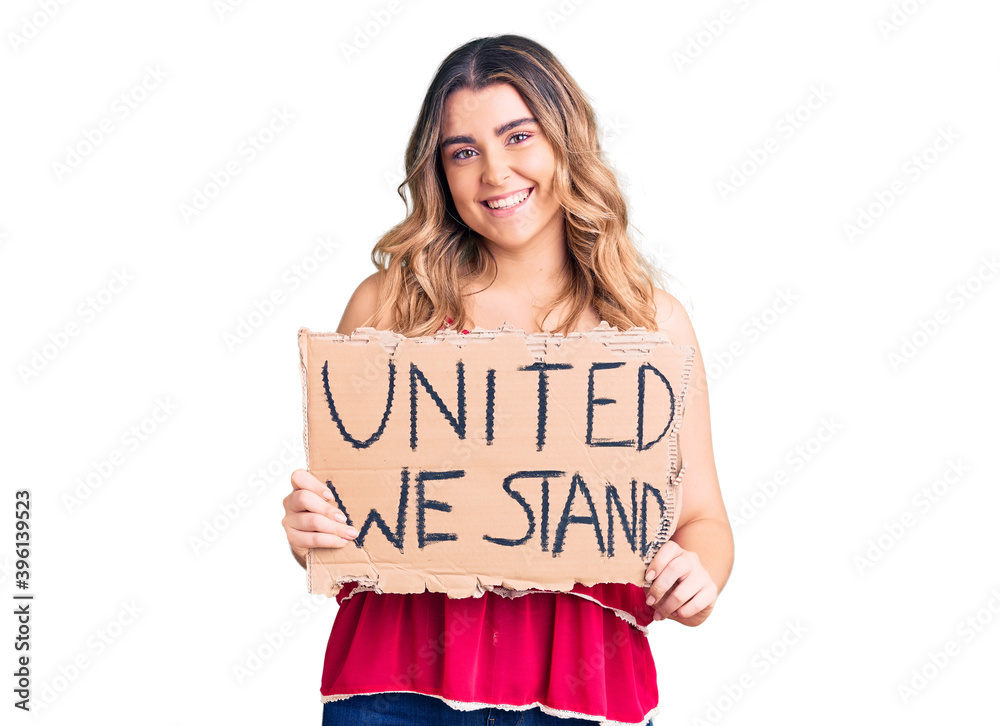 Young caucasian woman holding united we stand banner looking positive and happy standing and smiling with a confident smile showing teeth Young caucasian woman holding united we stand banner looking positive and happy standing and smiling with a confident smile showing teeth
