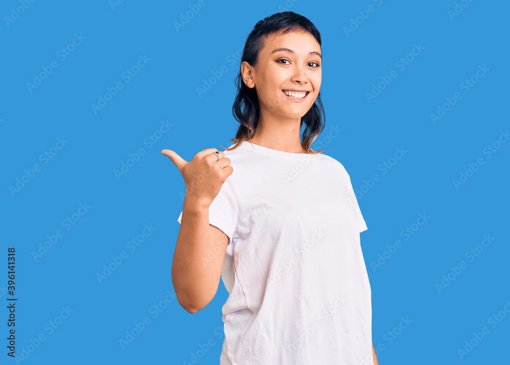 Young woman wearing casual clothes smiling with happy face looking and pointing to the side with thumb up. Young woman wearing casual clothes smiling with happy face looking and pointing to the side with thumb up.