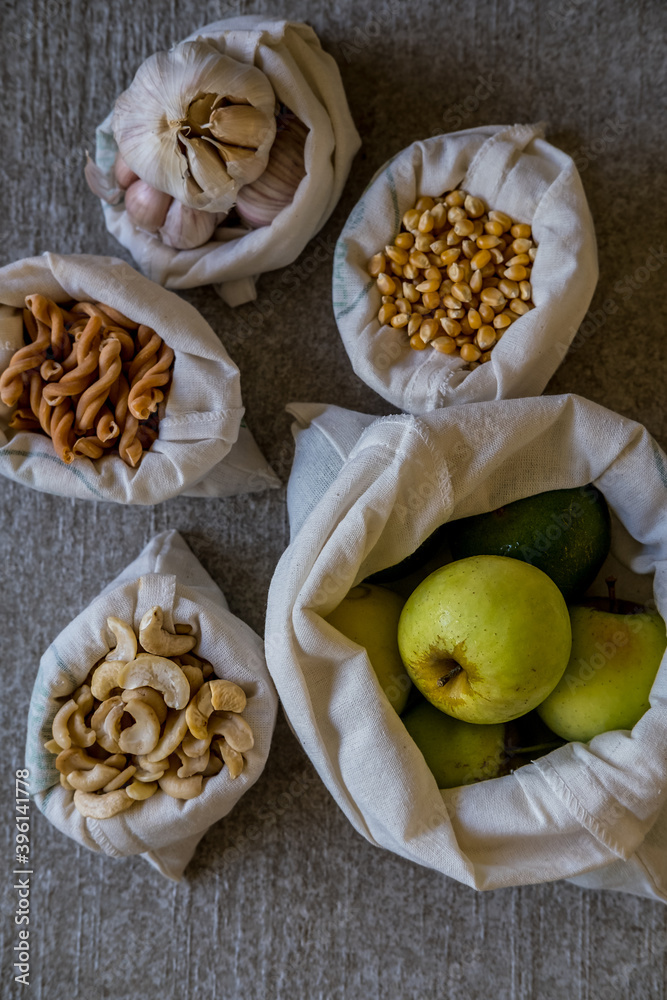 Fototapeta premium Variety of different groceries in cotton bags: pasta, nuts, grains, vegetables and fruits ready for storage. Eco-friendly organic bio kitchen products. Zero waste sustainable plastic free lifestyle