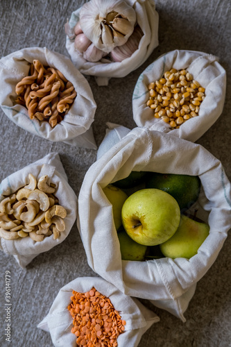 Variety of different groceries in cotton bags: pasta, nuts, grains, vegetables and fruits ready for storage. Eco-friendly organic bio kitchen products. Zero waste sustainable plastic free lifestyle