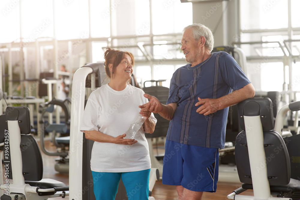 Positive happy senior people at gym. Cheerful elderly woman with bottle of water at fitness center. People, sport, healthy lifestyle.