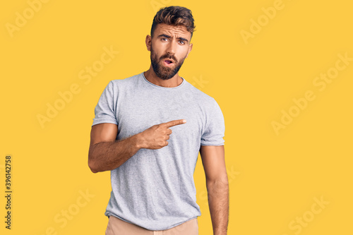 Young hispanic man wearing casual clothes surprised pointing with finger to the side, open mouth amazed expression.