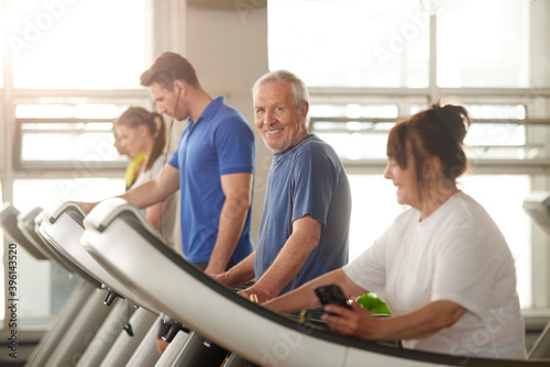 Old happy man runs on treadmill. People training at modern gym. Regular sports trainings help to keep fit and health.