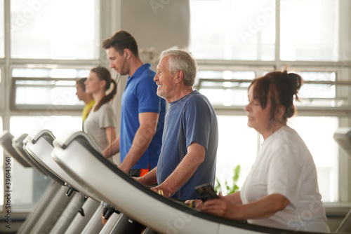 Indoor cardio workout. Elderly man and woman walking on treadmill, focus on man. Sport for seniors.