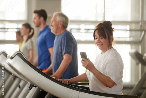People training on treadmills. Senior woman looking at smartphone during training at gym. People, sport, interet and modern technology.