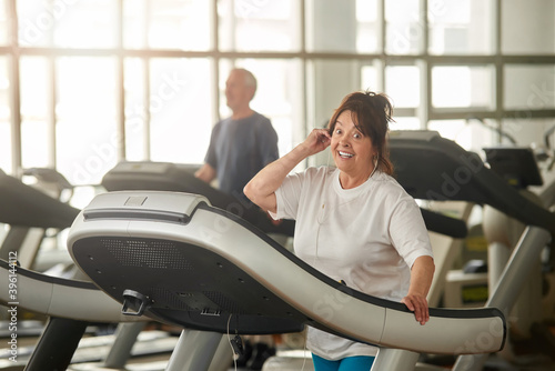 Excited senior woman on treadmill in gym. Happy eldrly woman working out at fitness club. Sport gives energy. photo