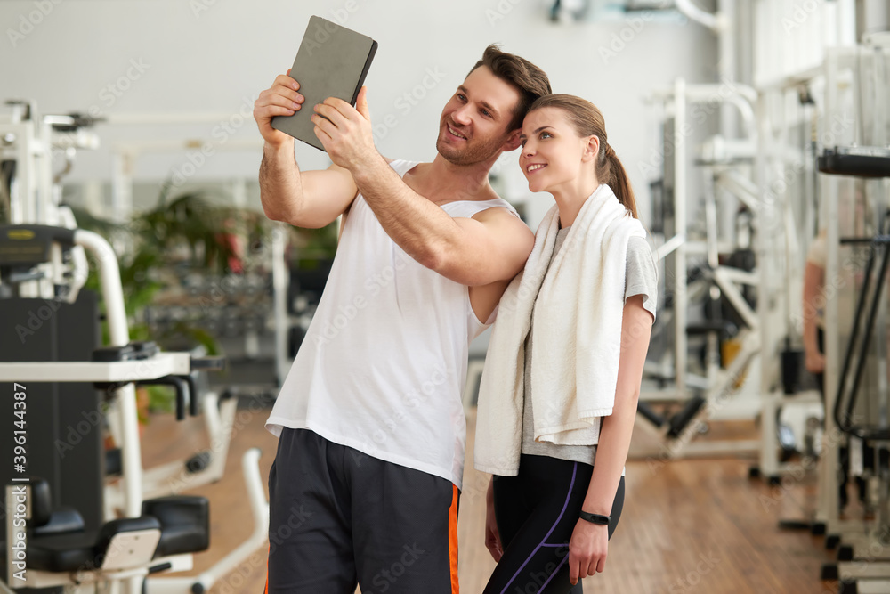 Young sporty couple taking selfie with tablet device. Cute athletic couple using digital tablet at gym. People, sport, training and modern technology concept. Young sporty couple taking selfie with tablet device. Cute athletic couple using digital tablet at gym. People, sport, training and modern technology concept.