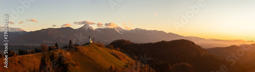 Panorama of golden sunrise at Jamnik, Slovenia with mountains behind the church