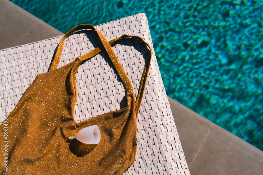 Silicone menstrual cup with bikini swimsuit by the pool with blue water