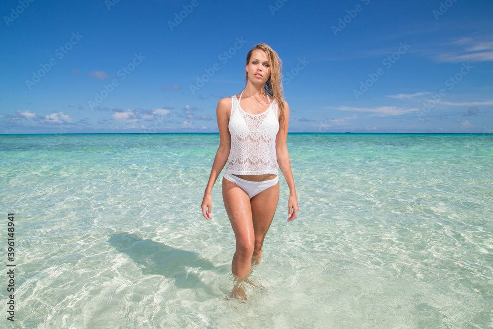 Beautiful slender girl in a white swimsuit at the sea on the beach in the Maldives