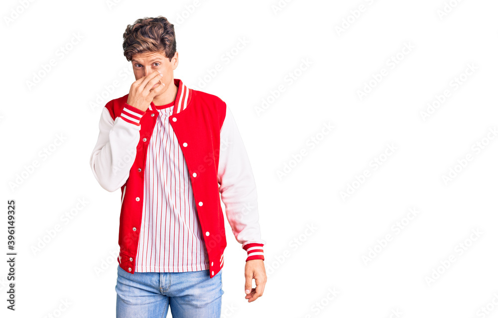 Young handsome man wearing baseball uniform smelling something stinky and disgusting, intolerable smell, holding breath with fingers on nose. bad smell Young handsome man wearing baseball uniform smelling something stinky and disgusting, intolerable smell, holding breath with fingers on nose. bad smell