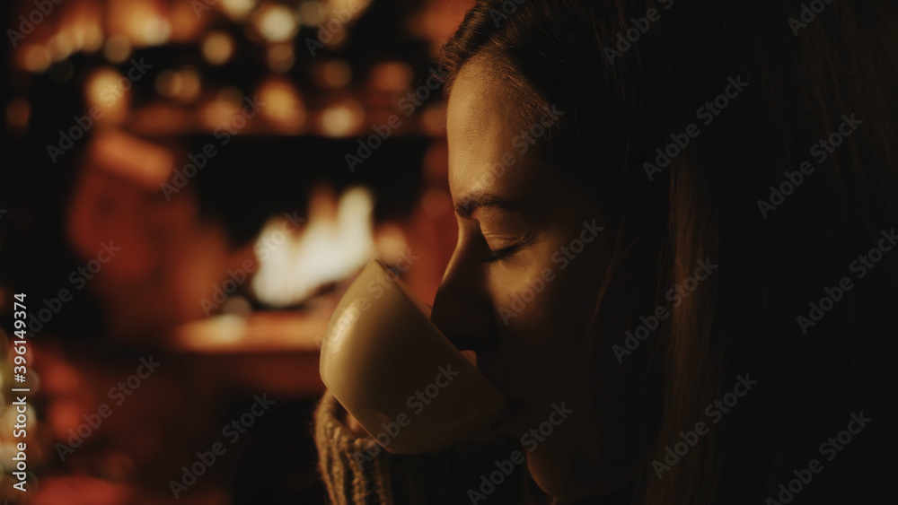 Beautiful romantic girl with cup of coffee or tea. Beautiful girl is enjoying coffee. Festive interior with lights, Christmas tree and fireplace in the background. Winter evening, cozy. Soft focus Beautiful romantic girl with cup of coffee or tea. Beautiful girl is enjoying coffee. Festive interior with lights, Christmas tree and fireplace in the background. Winter evening, cozy. Soft focus