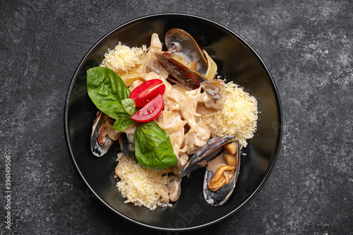 Pasta with seafood, mussels, scallop, rapana and cheese, on a black plate